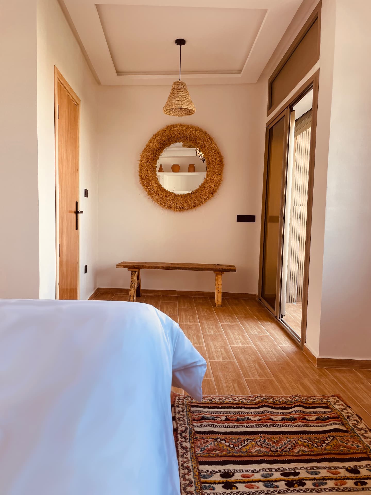 Miroir en raphia, banc en bois brut et tapis berbère dans la chambre