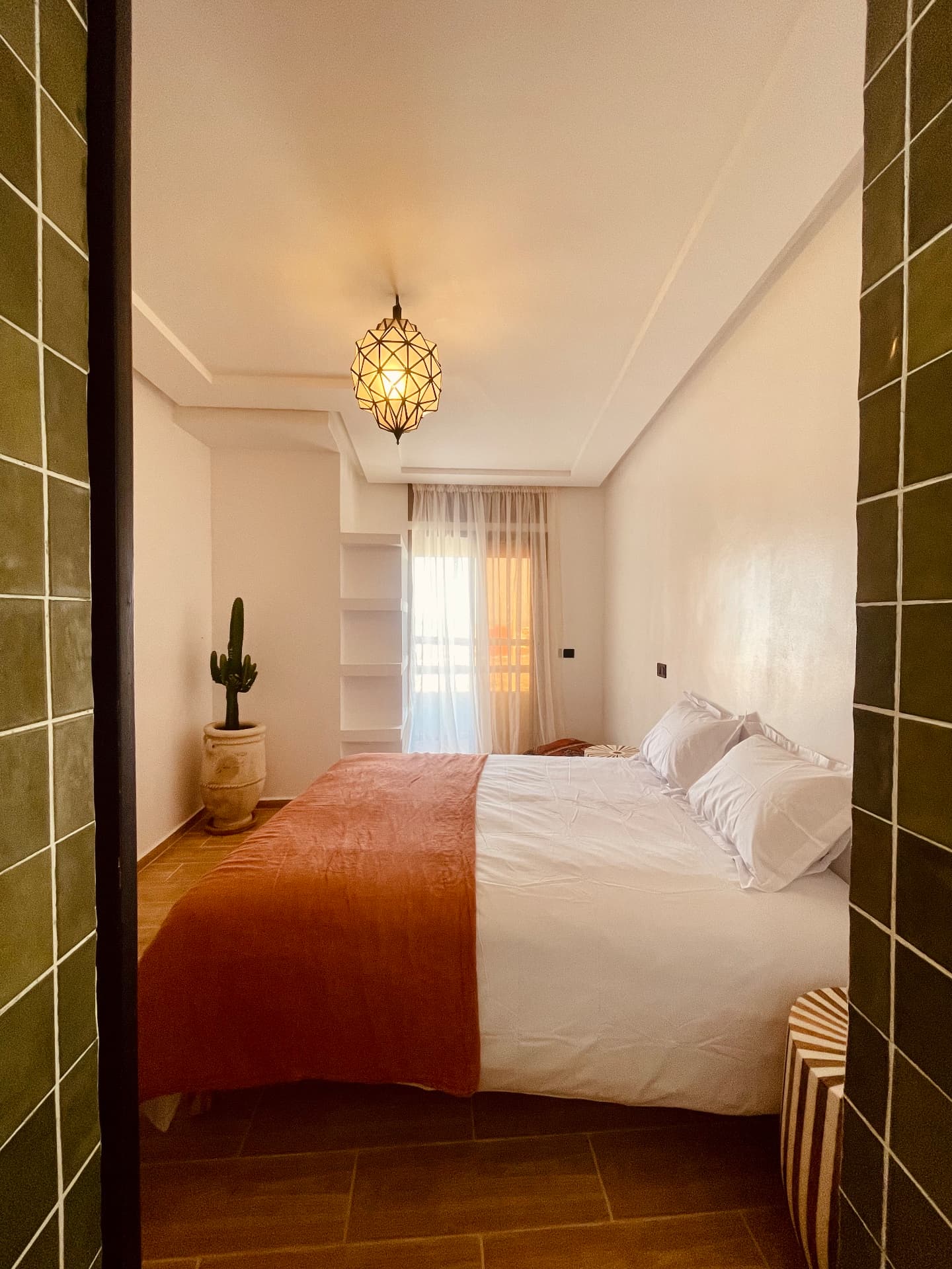 Chambre lumineuse aux murs à la chaux, lit blanc, plaid terracotta et zellige vert olive